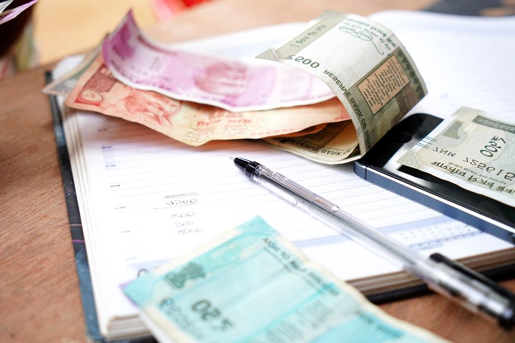 A person planning monthly expenses with a notebook, calculator and laptop at a tidy desk.
